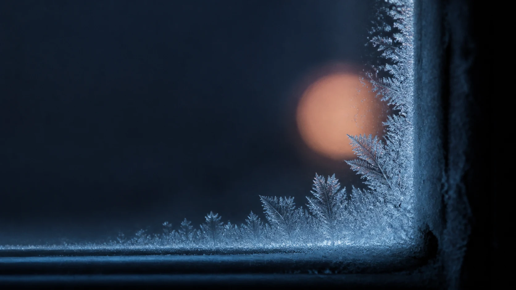 Frost forming on window glass with warm light beyond