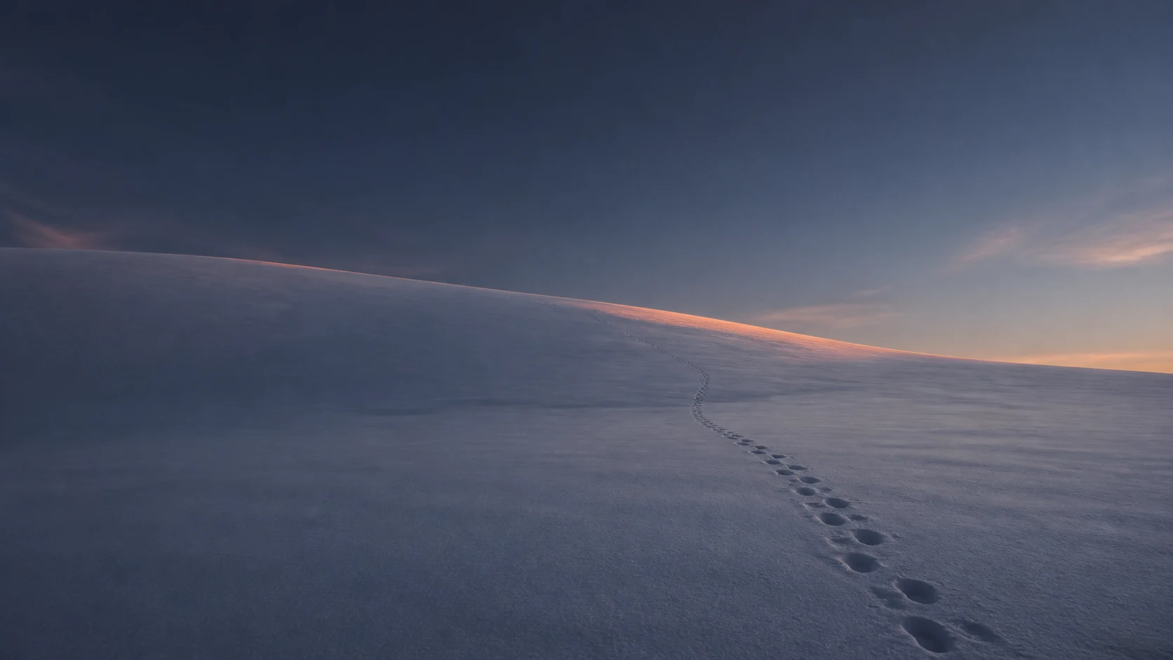 Boot tracks crossing an empty snowfield at dusk